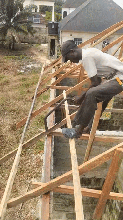 Construction worker cuts wood atop unfinished building in Nigeria