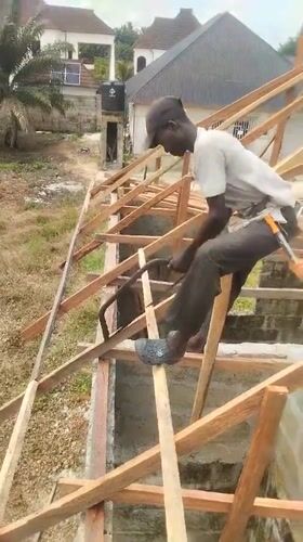 Construction worker cuts wood atop unfinished building in Nigeria