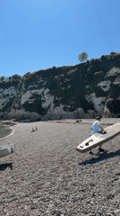 Man prepares sailboat and paddle board on Devon beach
