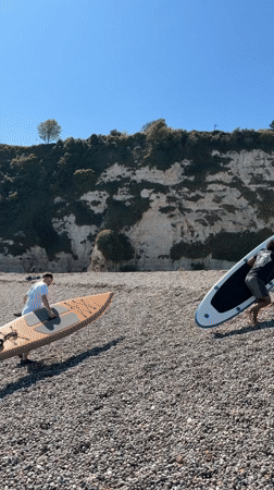 Man prepares sailboat and paddle board on Devon beach