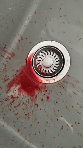 The video shows a close-up view of a sink drain covered in what appears to be blood. The blood is splattered around the drain and on the surrounding sink surface. The drain itself is a silver metal grate.