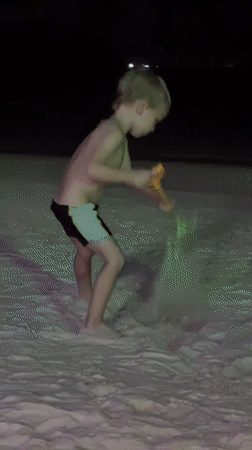 Child digs in sand on dimly lit Koh Phangan beach