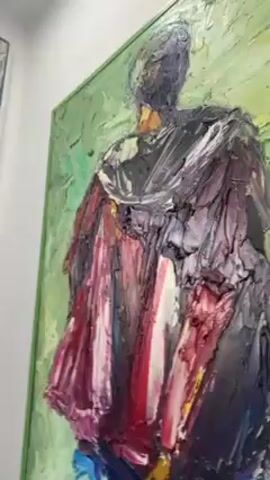 The video pans across a wall displaying various paintings. The first painting features a figure in dark clothing with splashes of red and blue. Next to it is a painting with a black and gray abstract pattern and a red dot in the upper corner. Then the camera focuses on a few other paintings including one with people and a motorcycle, a city scene with vehicles, and a portrait of two smiling individuals with short hair. A window is visible at the top of the screen, providing natural light.