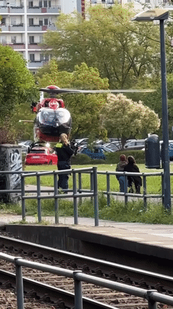 Red and white helicopter lands near Berlin train tracks with ground crew