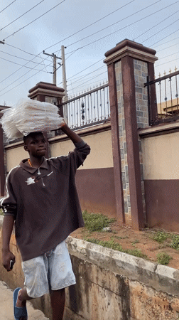 Man carries plastic bundle on head in Onitsha street scene