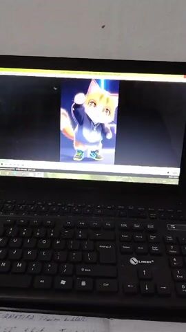 A video shows a laptop with an open media player, displaying an animation of a cat character. The cat is orange and white with large eyes, wearing a blue hoodie and sneakers. The background features blue neon lights. The laptop is black and sits on a surface with a piece of paper containing handwritten notes visible below the keyboard. The sound of music plays from the laptop.