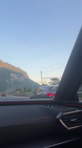 Vehicle travels Swiss highway near mountains, parallel train tracks