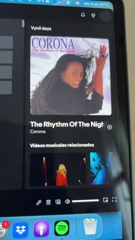The video displays a tablet screen showing a Spotify interface. The album art for "The Rhythm Of The Night" by Corona is prominently featured at the top. Below the album art, the song title "The Rhythm Of The Night" and the artist "Corona" are visible. A section titled "Videos musicales relacionados" (related music videos) shows several thumbnail images of music videos. At the bottom of the screen, the Spotify app icon is visible in the dock, along with other app icons like Mail, Dropbox, and Apple Podcasts. The tablet's status bar at the top shows the time as 10:17, the date as Mar 9, and the battery level as 55%.