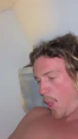 Here's a description of the video:

A shirtless man with a mustache and curly hair is lying down. He sticks his tongue out and makes a goofy face. He then touches his forehead with his finger while continuing to stick his tongue out.