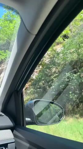 The video shows a view from inside a car, looking out the passenger side window. The window is partially open, and a side-view mirror is visible. Outside the window, there is a rocky hillside covered in green vegetation. The car appears to be moving, as indicated by the slight blur of the scenery and the changing perspective. The time stamp on the video indicates it was recorded on July 29, 2022, between 00:00 and 00:04. The lighting suggests it is daytime.