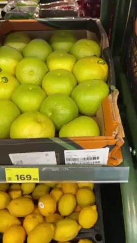 The video shows a carton of green and yellow sweety fruit in a grocery store. A yellow price tag below the carton displays the price of 169.99. Below the carton of sweety fruit, there is another carton of yellow lemons. The camera moves slightly, focusing on the price tag and then back to the sweety fruit.