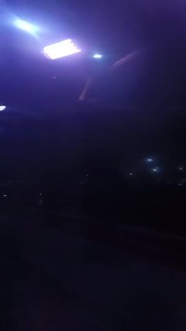 The video shows a street at night, illuminated by streetlights. The camera appears to be moving. Buildings and vegetation are visible in the background, though obscured by darkness. There's a roof or ceiling visible with a light fixture above.