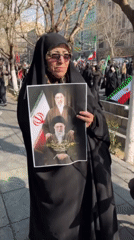Elderly woman holds photograph as men paint banner in Tehran