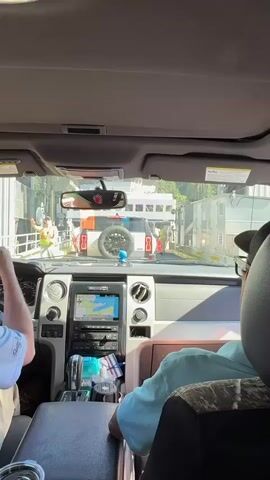 From inside a car, one man in a backwards cap and glasses turns in the passenger seat and says, "We did, we did just make it." He is wearing a teal shirt, and his seat has a camouflage pattern. The driver is wearing a light blue shirt. The car is on a ferry boat. In front of the car is another truck and a man in a yellow vest is directing traffic.