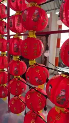 The video shows a dense array of red Chinese lanterns strung on metal frames. The lanterns are round with painted figures and Chinese characters. The frames are arranged to form a kind of tunnel or passage. Some light bulbs hang amongst the lanterns. Towards the end of the video, one person walks through the lantern display. The sky is visible between the lanterns and through the structures behind them. The video appears to have been taken outdoors.