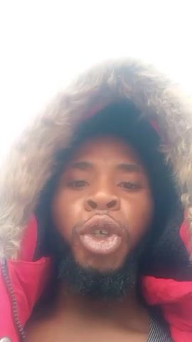 A man with a beard and wearing a red jacket with a fur-lined hood is looking directly at the camera. He points his finger forward and talks, saying "If you want to see something cool, you have to see this dam." The background is a bright, overcast sky.