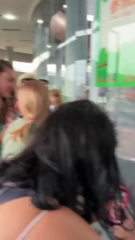The video shows a medium-sized brown monkey with long fur sitting on a glass surface inside of an enclosure. People are standing on the other side of the glass, looking at the monkey. Some people are holding up cellphones and taking pictures. The enclosure has a green background with what looks like painted trees or foliage. The scene appears to be at a zoo or wildlife park.