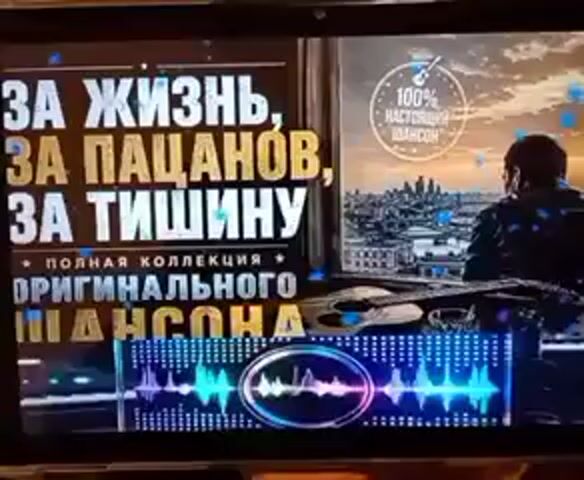 A screen displays a promotional image for a music collection. The text on the left reads "FOR LIFE, FOR GUYS, FOR SILENCE" and "COMPLETE COLLECTION OF ORIGINAL CHANSON". A circle with a guitar icon and "100% REAL CHANSON" is in the upper right. A man is silhouetted from behind, looking out over a city skyline. An acoustic guitar rests in the foreground. A colorful equalizer graphic is at the bottom of the screen.