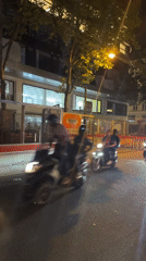 Two motorcycles pass through nighttime Paris street near construction