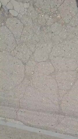 This is a close-up video of cracked asphalt pavement. The cracks are irregular and form a network across the surface. There are some small pebbles and debris visible within the cracks. The lighting is somewhat dim, suggesting it might be overcast or late in the day. No people or other objects are clearly visible.