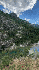Tourists cross rusty suspension bridge over turquoise Montenegro river