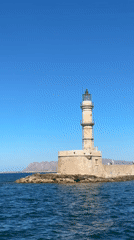 Sunny afternoon at a Greek coastal lighthouse with passing yachts