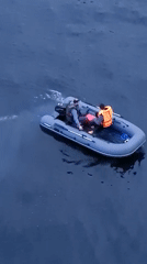 Inflatable boat with two aboard cuts across dark water
