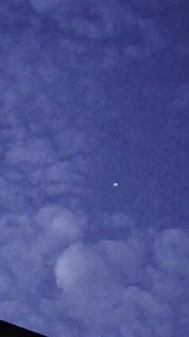The video shows a nighttime sky with clouds. A small, bright object with two distinct lights is visible in the center of the frame. The object appears to be stationary in the sky, and the camera remains focused on it as the sky darkens slightly.