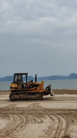 Construction equipment operates on Vietnam beach under cloudy skies