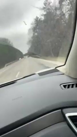 The video shows a car driving on a highway on a cloudy day. There are trees on either side of the road, and other cars can be seen in the distance. The view is from the front seat of the car, focusing on the road ahead.