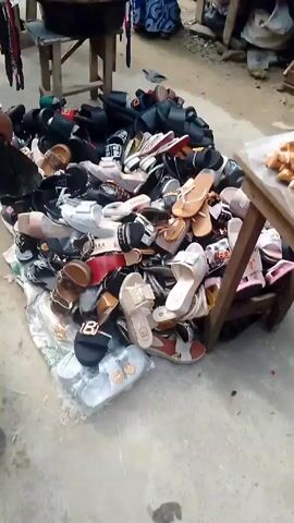 The video shows scenes from an outdoor market.

In the first scene, there is a pile of sandals and shoes, and in the background, there are clothes for sale on a stool. 

The second scene shows a collection of hats, also displayed on a stool, along with a pile of sandals.

The third scene shows an array of plates piled high with red tomatoes and red peppers, likely for sale. People are walking by the produce stand.

The final scene features the tomato and pepper stand along with other items being sold, including brightly-colored, individually-wrapped plastic spoons and other small goods. There are several people in the background, some sitting and others browsing the market.