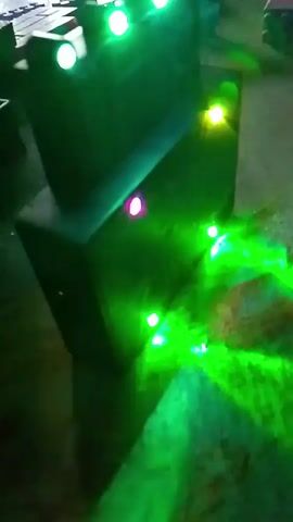 The video shows a close-up, shaky view of a dark, black, tower-like object with multiple colored LED lights embedded in it. The lights cycle through various colors, including blue, green, yellow, red, and pink, casting beams of light onto the surrounding floor and surfaces, creating a somewhat blurry and abstract visual effect. The object appears to be made of stacked rectangular blocks. The lighting suggests a dimly lit environment.