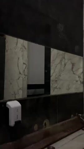 The video shows the inside of a restroom with black and white marble walls. There is a sink and a white hand sanitizer dispenser attached to the wall. The camera pans across the walls and to a corner where black stripes are painted onto the white wall.