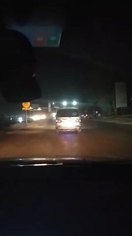 A car is driving at night on a multi-lane road. Ahead, a white van drives in the same direction. Other cars are visible on the road. Streetlights illuminate the scene. The video is shot from inside the car, looking out through the windshield.