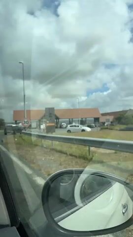 The video begins with a shot of a gas station from inside a vehicle. The gas price board shows the price of SP95-E10 at 1.990, SP95 at 1.9, E85 at 0.823, and Diesel at 2.139. A speed limit sign of 30 is visible. As the vehicle moves forward, a gas station with a "Total Energies" sign comes into view. Several cars and a truck are at the gas pumps. The video captures the entrance to the gas station, showing the canopy, pumps, and various signs. A person is seen fueling a vehicle. The weather appears to be cloudy with some sunlight breaking through.