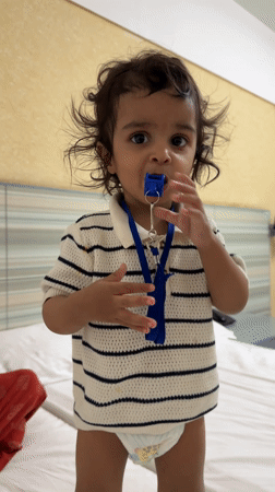 Toddler plays with whistle while standing on bed in India