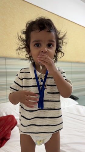 Toddler plays with whistle while standing on bed in India