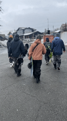 Five snowboarders walk single file on asphalt road
