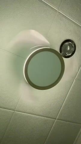 A ceiling fan is spinning above a tiled ceiling. A light is integrated into the fan. The fan is creating a hazy effect around its blades due to its rotation.