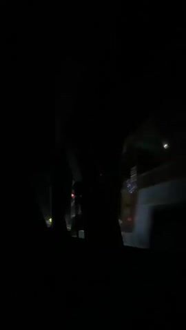The video shows a view from inside a car at night. The camera is looking out the side window. The window frame is visible in the foreground. Outside the window, there are trees and streetlights. The car appears to be moving. There is a reflection in the window, but it is unclear what it is. The overall impression is one of a nighttime drive.