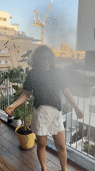 Woman cools off with hose on plant-filled balcony in Israel