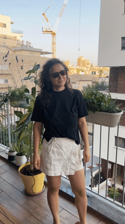 Woman cools off with hose on plant-filled balcony in Israel