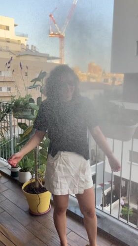 Woman cools off with hose on plant-filled balcony in Israel