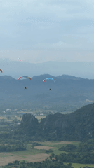Three paragliders soaring over misty Laos mountain terrain