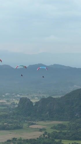 Three paragliders soaring over misty Laos mountain terrain