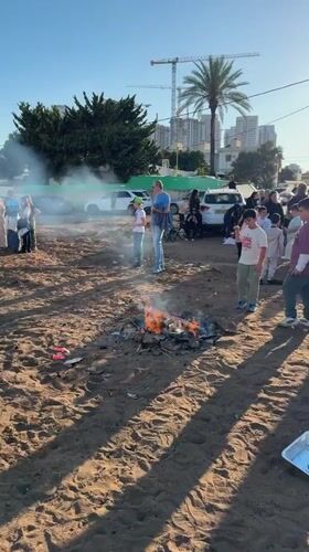 Children gather around bonfires on sandy lot in Netanya