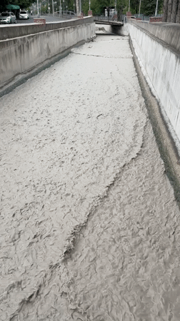 Drainage channel surging with thick, turbulent muddy water