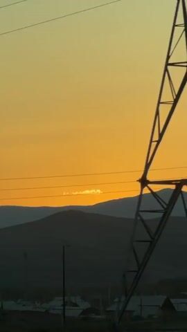 A time lapse video shows the sun setting behind silhouetted mountains and power lines. The sky is a gradient of yellow and orange.