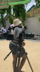 Film crew shoots outdoor scenes under umbrellas on sunny day