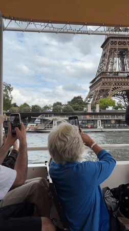 Tourists cruise Seine River, photograph Eiffel Tower on cloudy Monday
